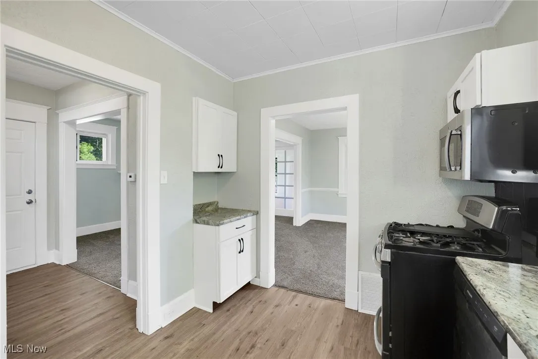 Kitchen with appliances with stainless steel finishes, ornamental molding, light wood-style flooring, white cabinetry, and baseboards