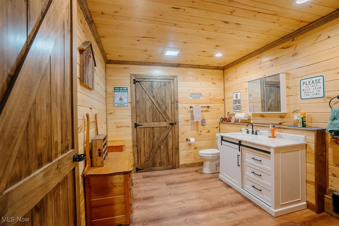Bathroom featuring wooden ceiling, vanity, toilet, wood walls, and wood finished floors