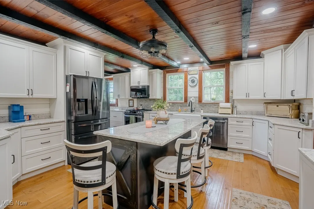 Kitchen featuring appliances with stainless steel finishes, wooden ceiling with exposed beams, light wood-style floors, a breakfast bar area, and a sink