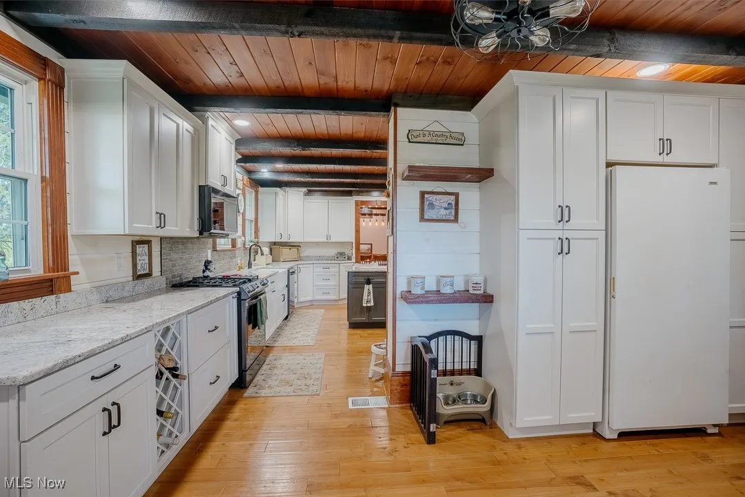 Kitchen with freestanding refrigerator, range with gas cooktop, white cabinetry, wood ceiling with exposed beams, and stainless steel microwave