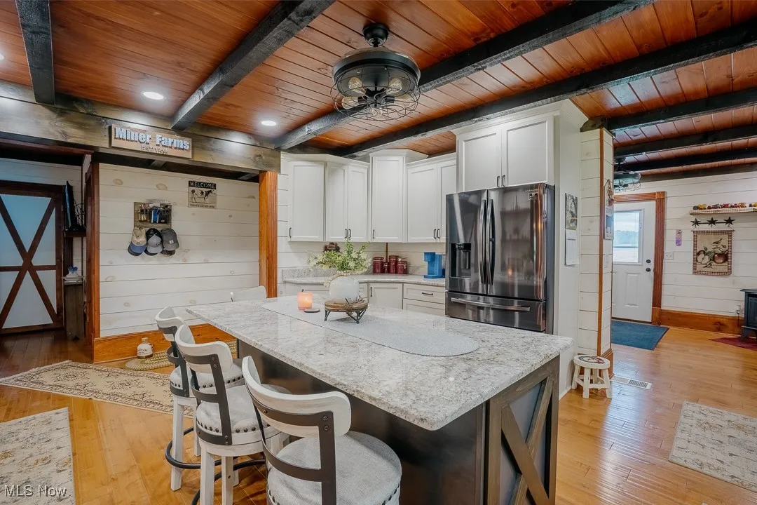 Kitchen featuring stainless steel fridge with ice dispenser, wooden ceiling with exposed beams, wooden walls, light wood-style floors, and white cabinetry