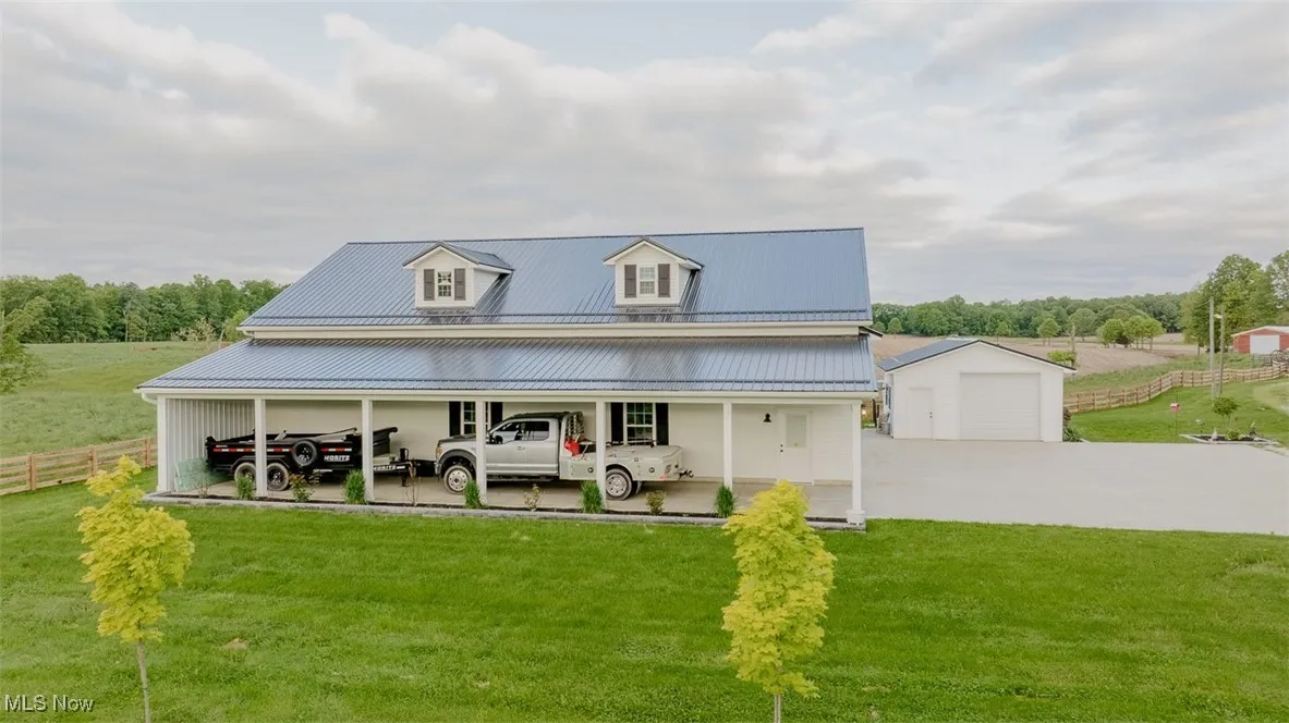 View of front facade featuring driveway, metal roof, an outbuilding, and a garage