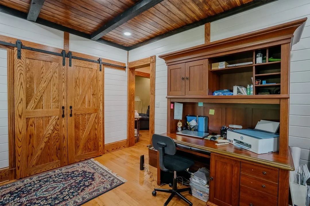 Office area with wood ceiling with exposed beams, light wood-type flooring, wood walls, a barn door, and built in study area