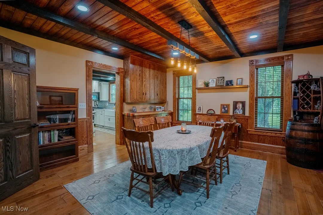 Dining room featuring wooden ceiling with exposed beams, light wood-style flooring, healthy amount of natural light, and a wainscoted wall