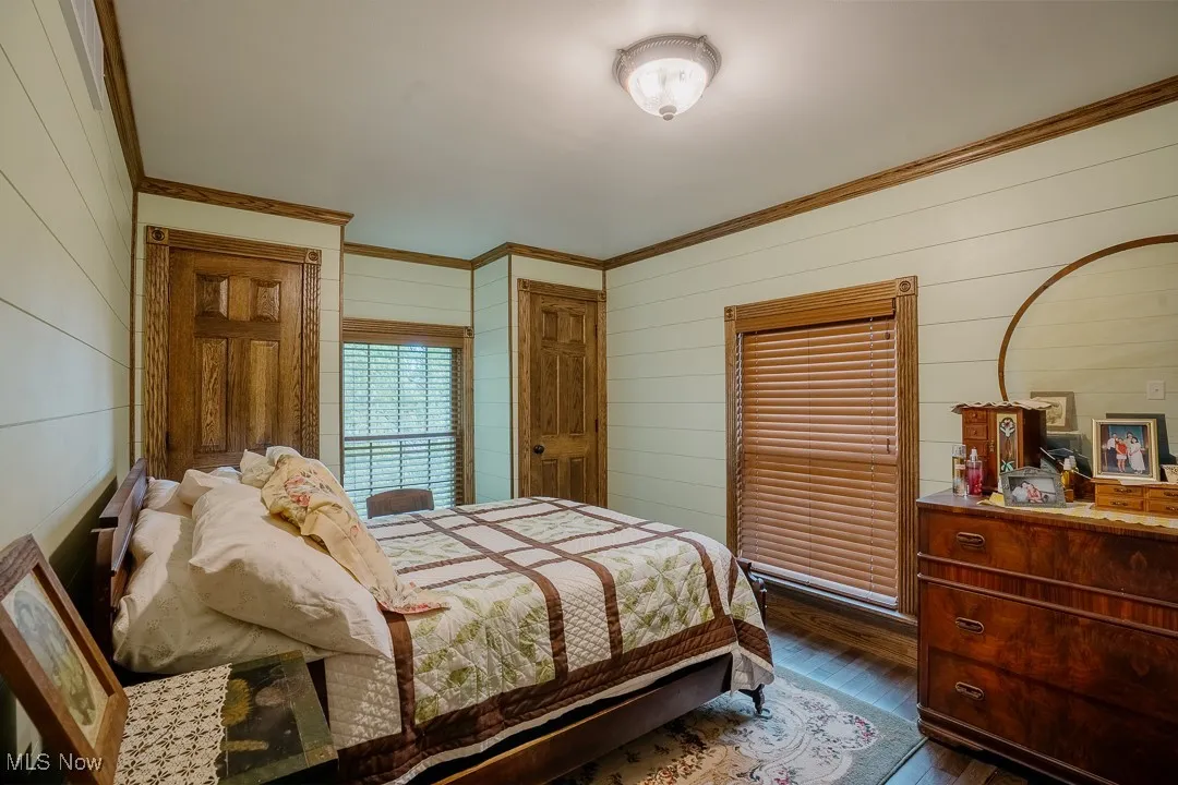 Bedroom featuring wood walls, crown molding, and dark wood-style floors