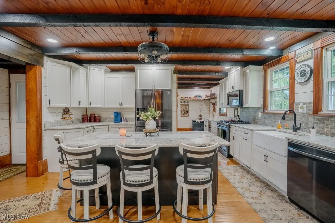 Kitchen featuring appliances with stainless steel finishes, wood ceiling with exposed beams, light stone countertops, light wood-style floors, and tasteful backsplash