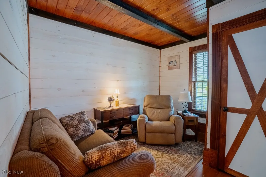 Sitting room featuring wood walls, wooden ceiling with exposed beams, and wood finished floors