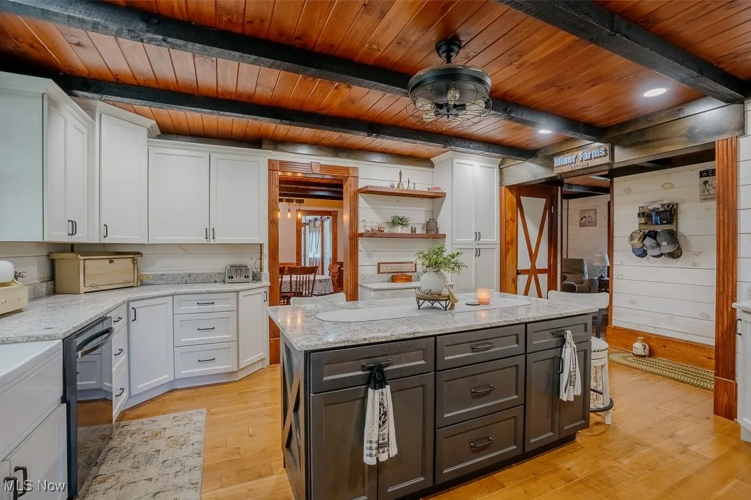 Kitchen featuring wooden ceiling with exposed beams, white cabinetry, dishwasher, light wood finished floors, and light stone counters