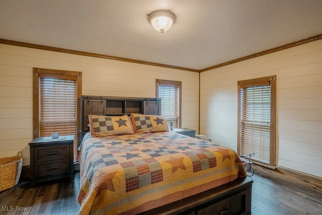 Bedroom with hardwood / wood-style floors, wooden walls, and crown molding