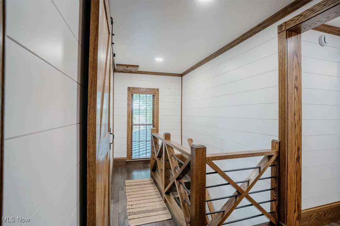 Hallway with wood finished floors, an upstairs landing, crown molding, wooden walls, and recessed lighting