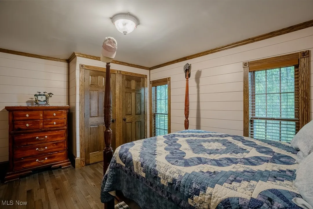Bedroom with multiple windows, dark wood-style floors, wooden walls, and ornamental molding