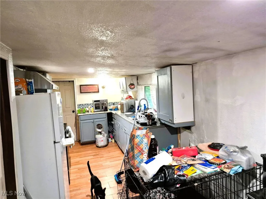 Kitchen featuring gray cabinets, freestanding refrigerator, light wood-type flooring, light countertops, and a textured ceiling