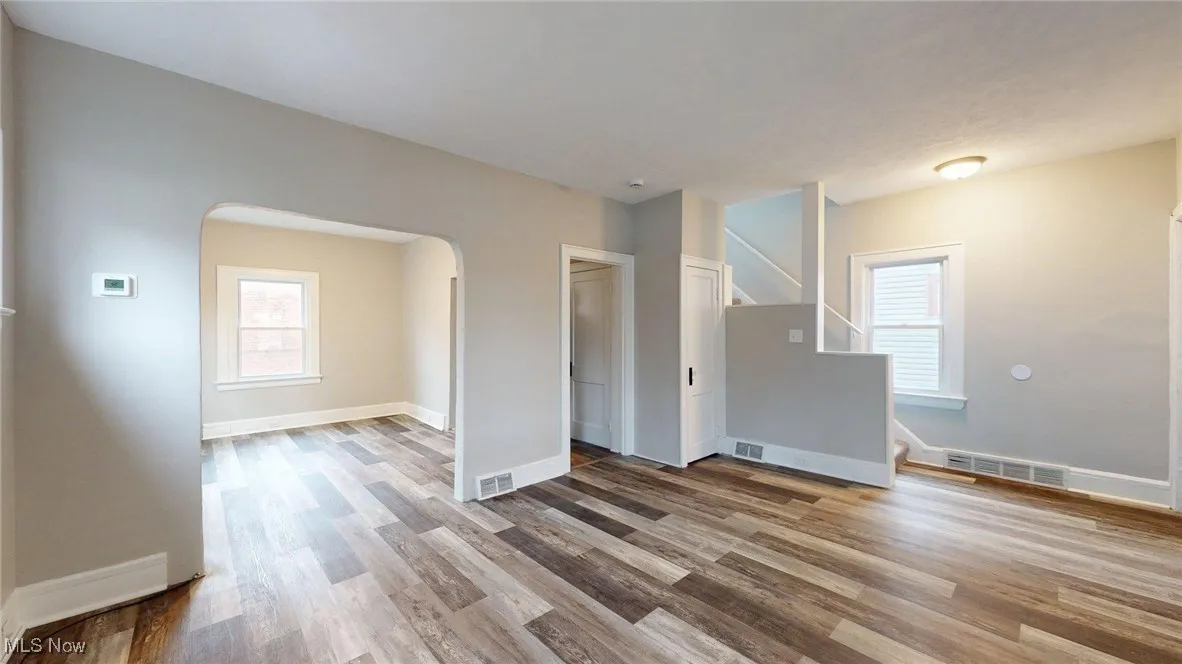 Empty room with arched walkways, wood finished floors, visible vents, and stairs