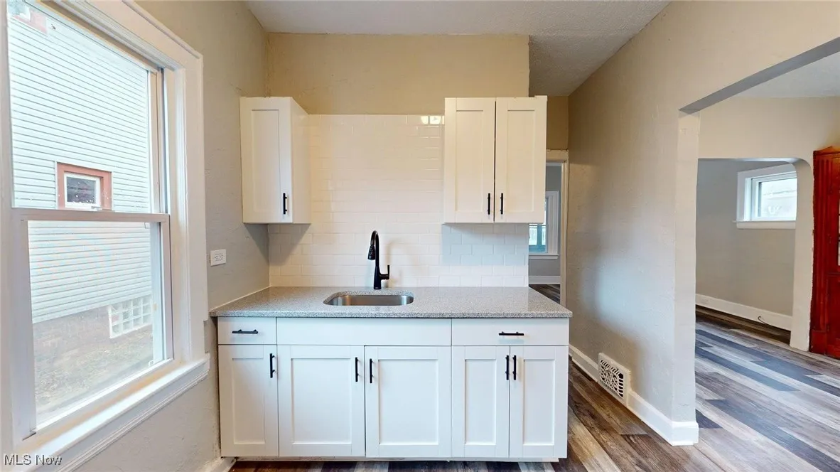 Kitchen with white cabinets, dark wood-style floors, visible vents, a sink, and tasteful backsplash