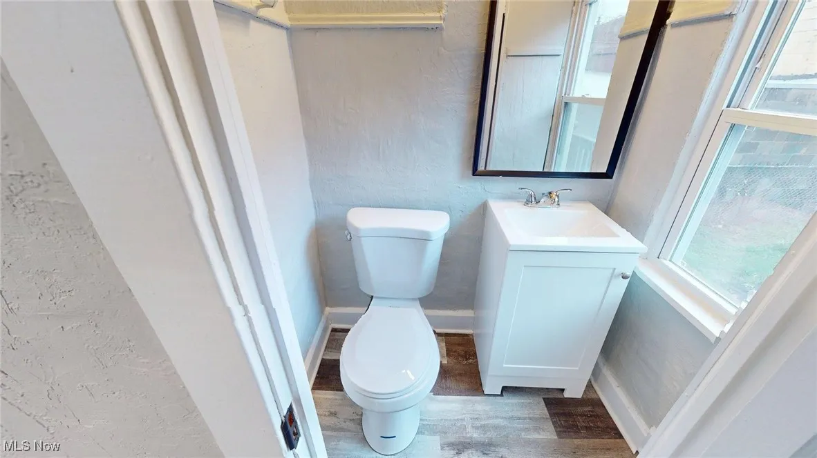 Half bathroom featuring toilet, a textured wall, and plenty of natural light