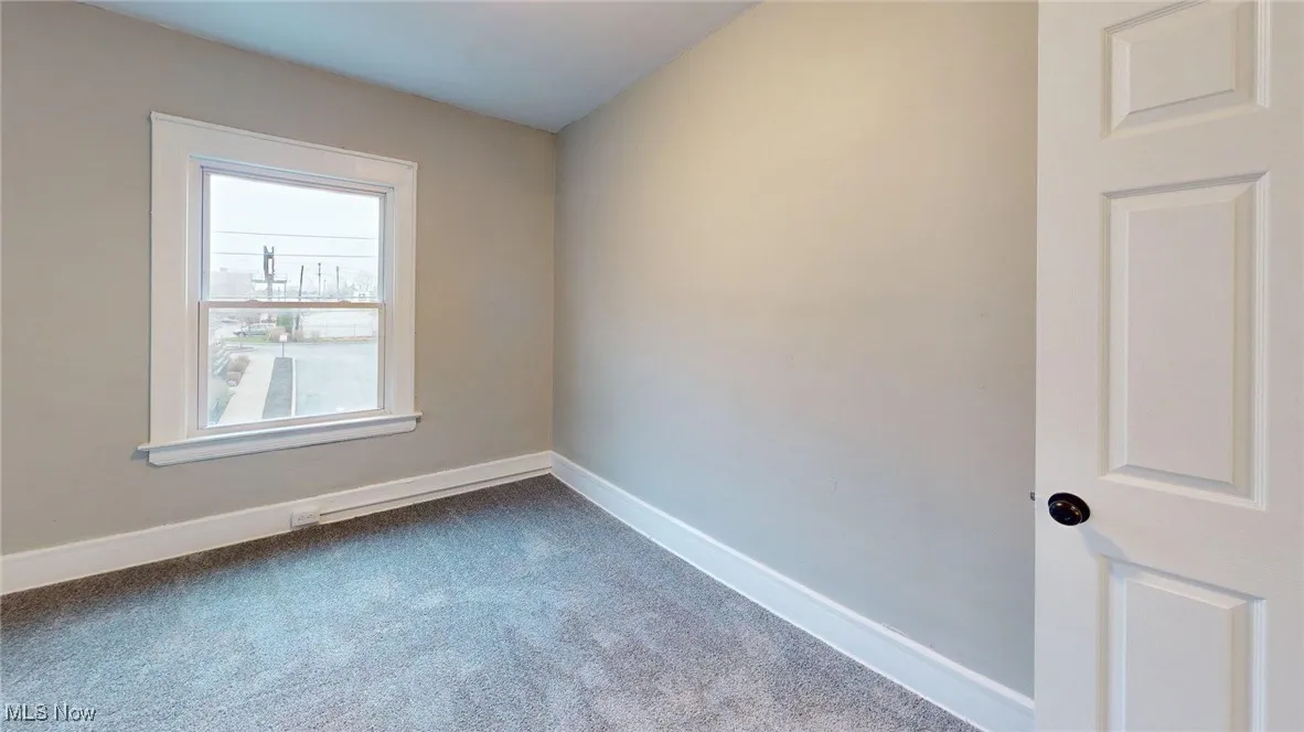Unfurnished room featuring dark colored carpet and baseboards