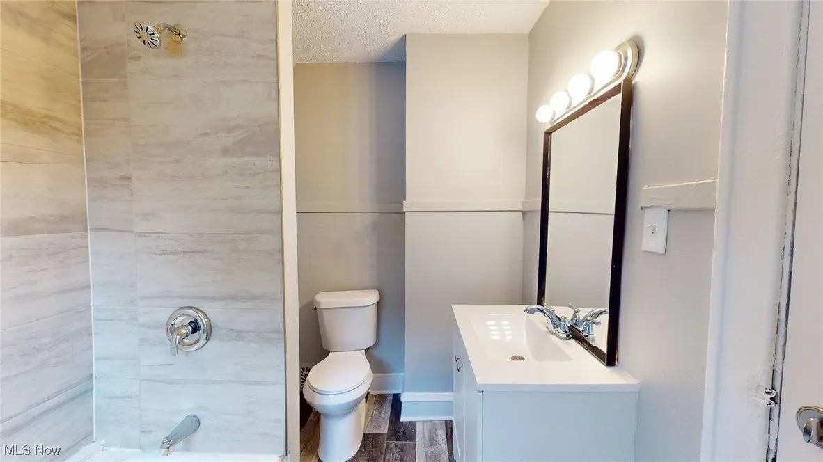 Full bath with toilet, vanity, wood finished floors, and a textured ceiling