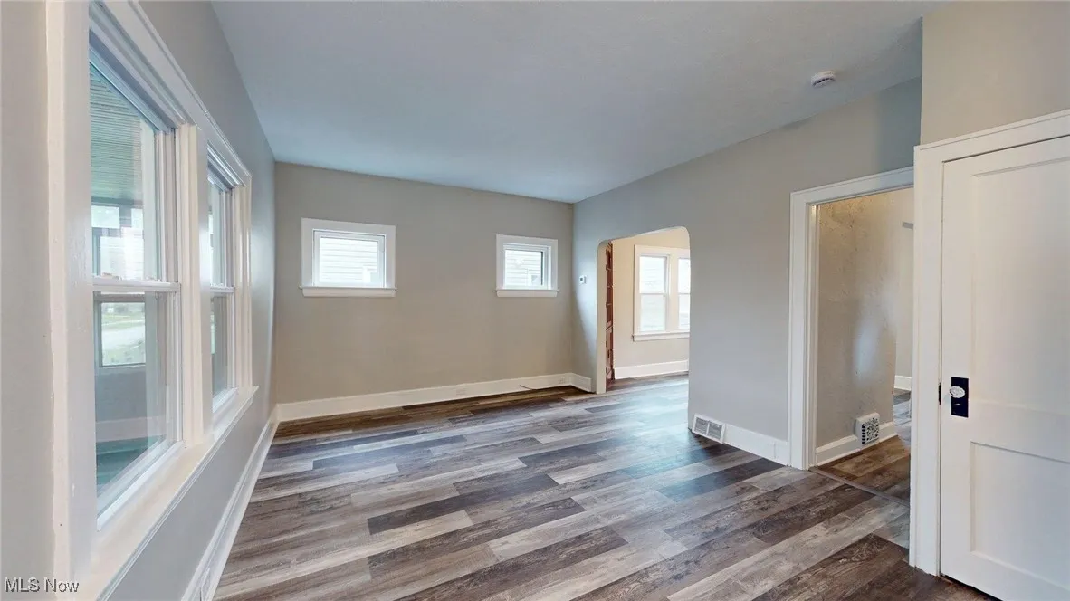 Spare room featuring arched walkways, dark wood finished floors, baseboards, and visible vents
