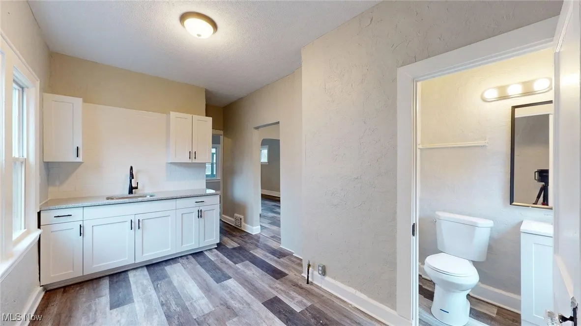 Kitchen with wood finished floors, a sink, a textured wall, light countertops, and white cabinetry