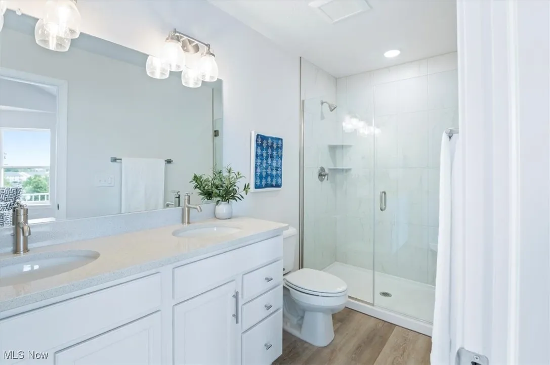 Full bath with a shower stall, toilet, double vanity, and wood finished floors