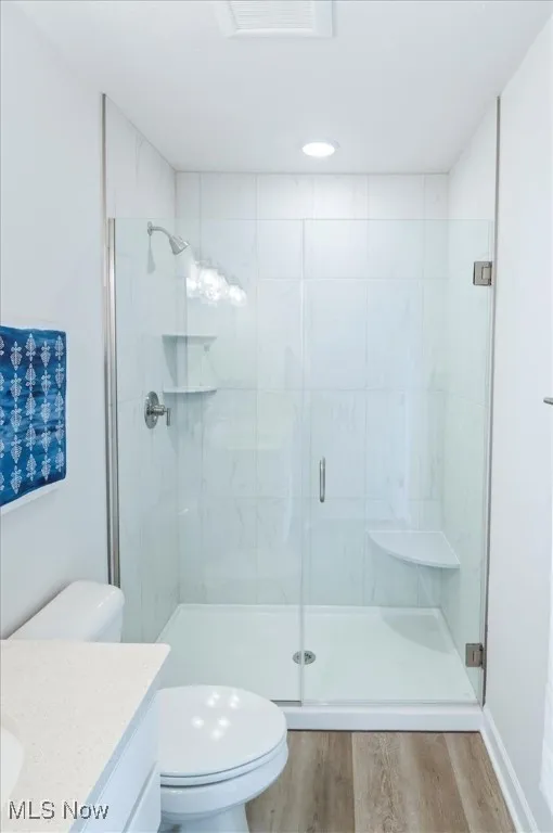 Bathroom with toilet, wood finished floors, vanity, and a stall shower
