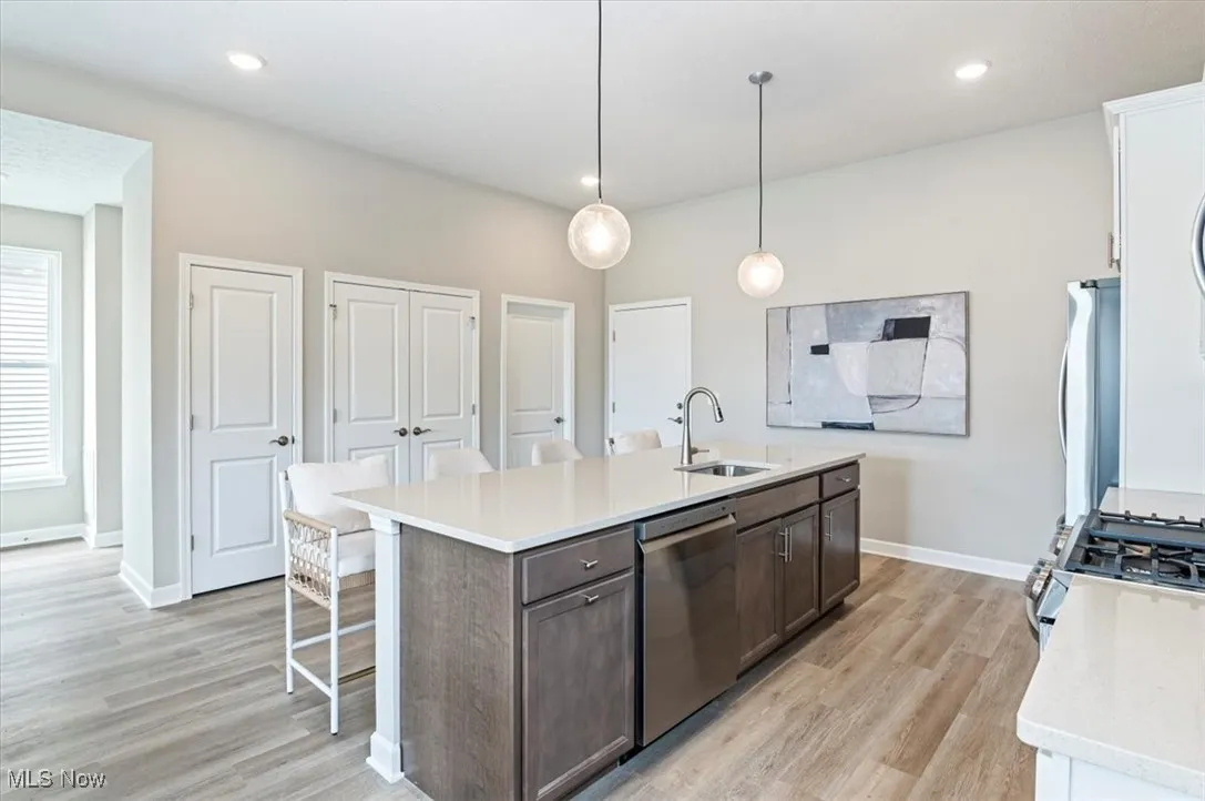 Kitchen with stainless steel appliances, a sink, light wood-type flooring, light countertops, and a center island with sink