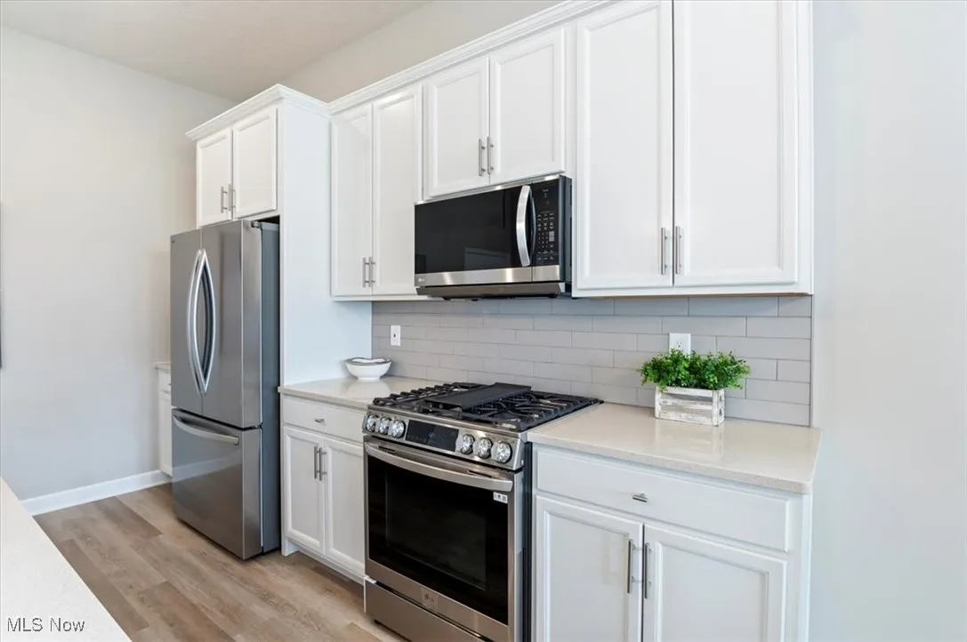 Kitchen featuring appliances with stainless steel finishes, light wood finished floors, light countertops, white cabinets, and tasteful backsplash