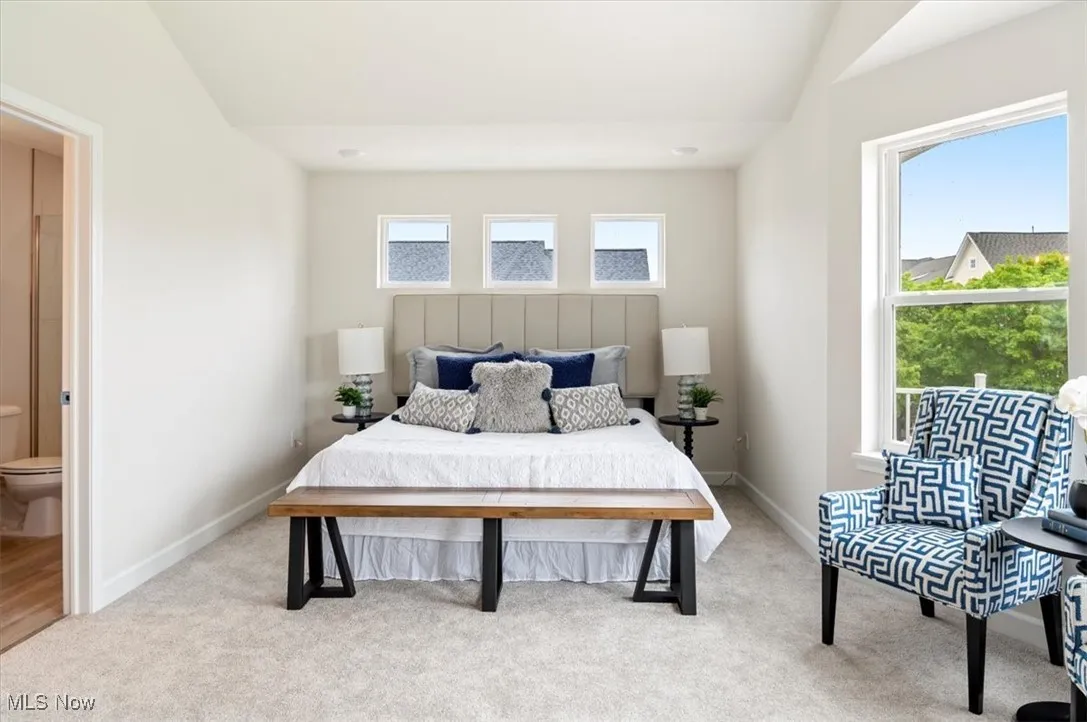 Bedroom with light carpet, baseboards, lofted ceiling, and ensuite bathroom