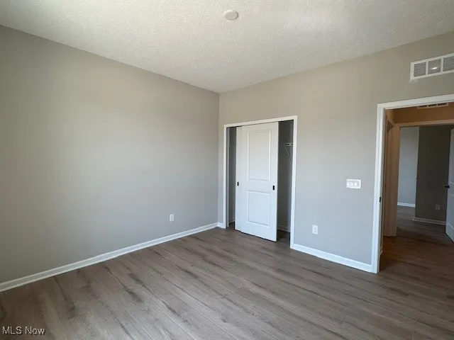 Unfurnished bedroom with a textured ceiling, wood finished floors, and a closet