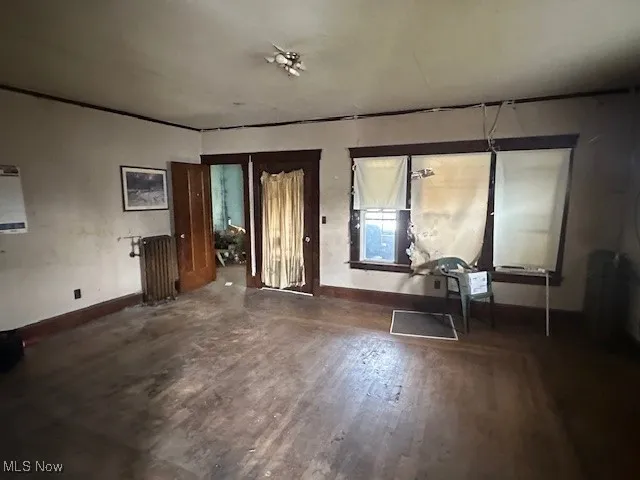 Unfurnished living room featuring wood finished floors, baseboards, and radiator