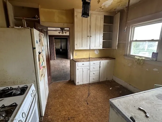 Kitchen featuring white range with gas cooktop, open shelves, white cabinetry, a ceiling fan, and light countertops