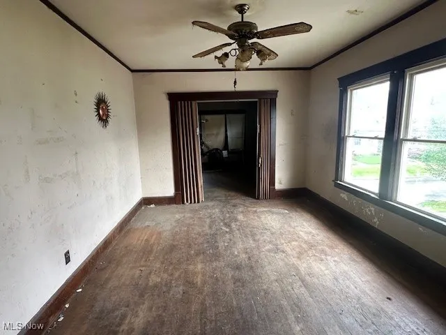 Empty room with baseboards, ornamental molding, ceiling fan, and wood finished floors