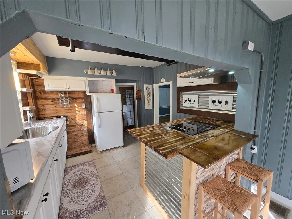 Kitchen with freestanding refrigerator, white cabinets, wooden walls, black electric cooktop, and a sink