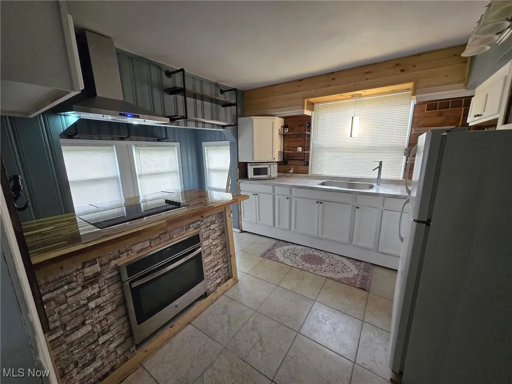 Kitchen featuring freestanding refrigerator, black electric cooktop, white cabinetry, stainless steel oven, and a sink