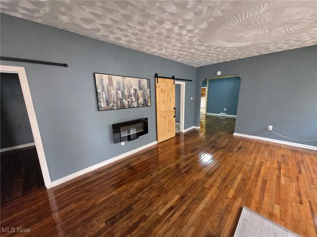 Unfurnished living room with wood-type flooring, a barn door, arched walkways, baseboards, and a textured ceiling