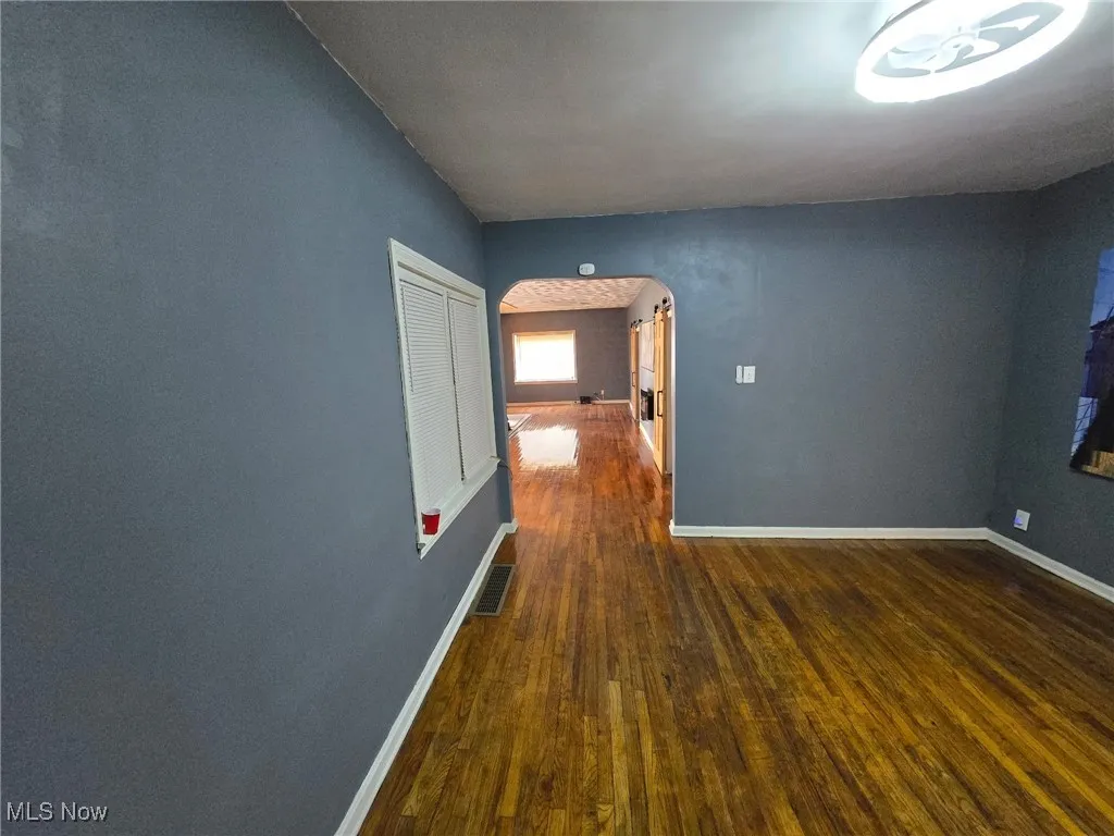 Unfurnished room with arched walkways, hardwood / wood-style flooring, and baseboards