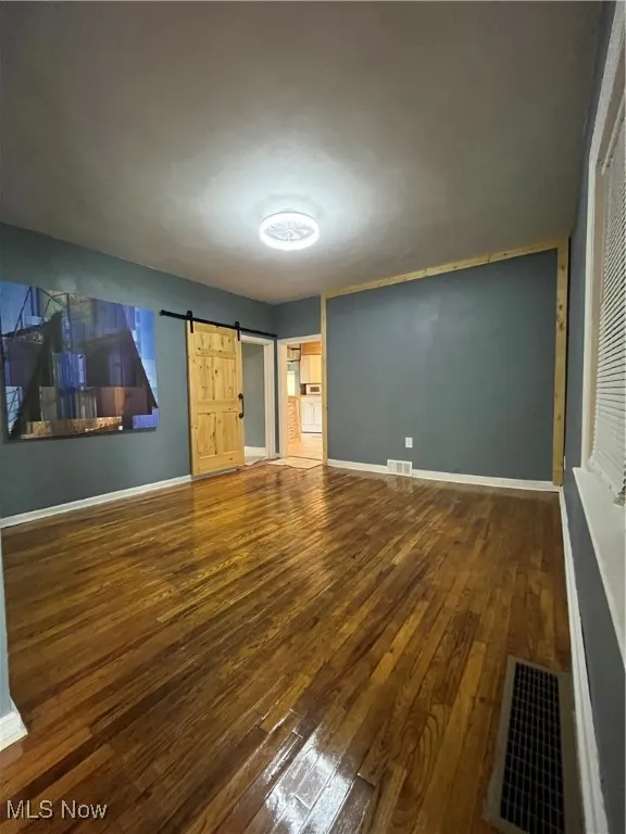 Unfurnished bedroom featuring hardwood / wood-style floors, baseboards, and a barn door