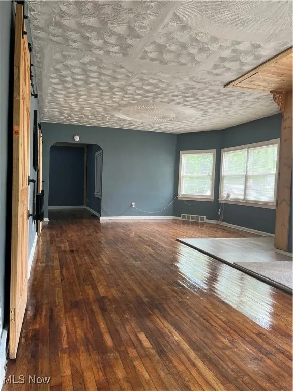 Unfurnished room with arched walkways, hardwood / wood-style floors, and baseboards