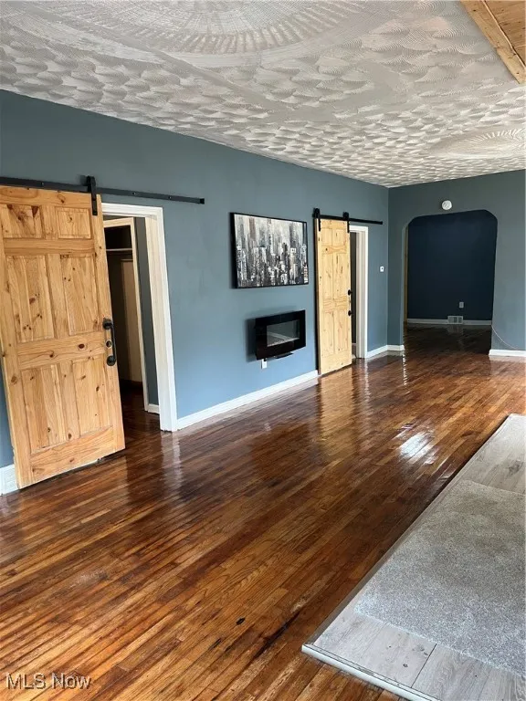Unfurnished living room with a barn door, arched walkways, hardwood / wood-style flooring, and baseboards
