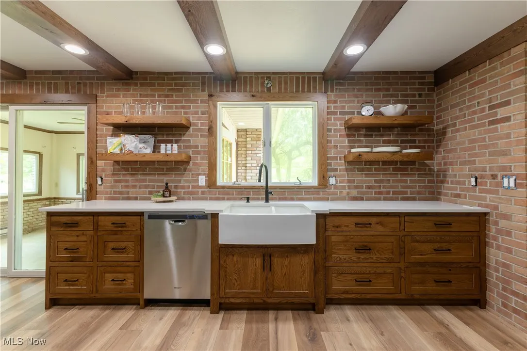 Kitchen featuring stainless steel dishwasher, open shelves, a sink, light countertops, and beamed ceiling