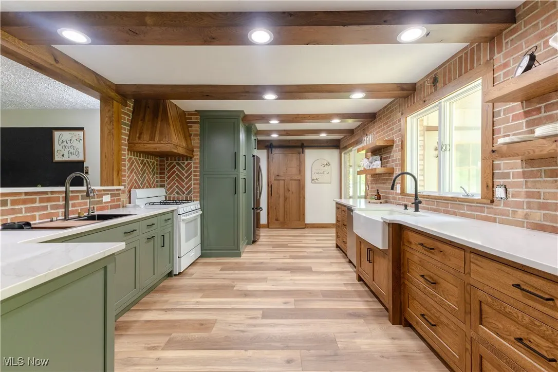 Kitchen featuring green cabinetry, gas range gas stove, a sink, premium range hood, and beamed ceiling