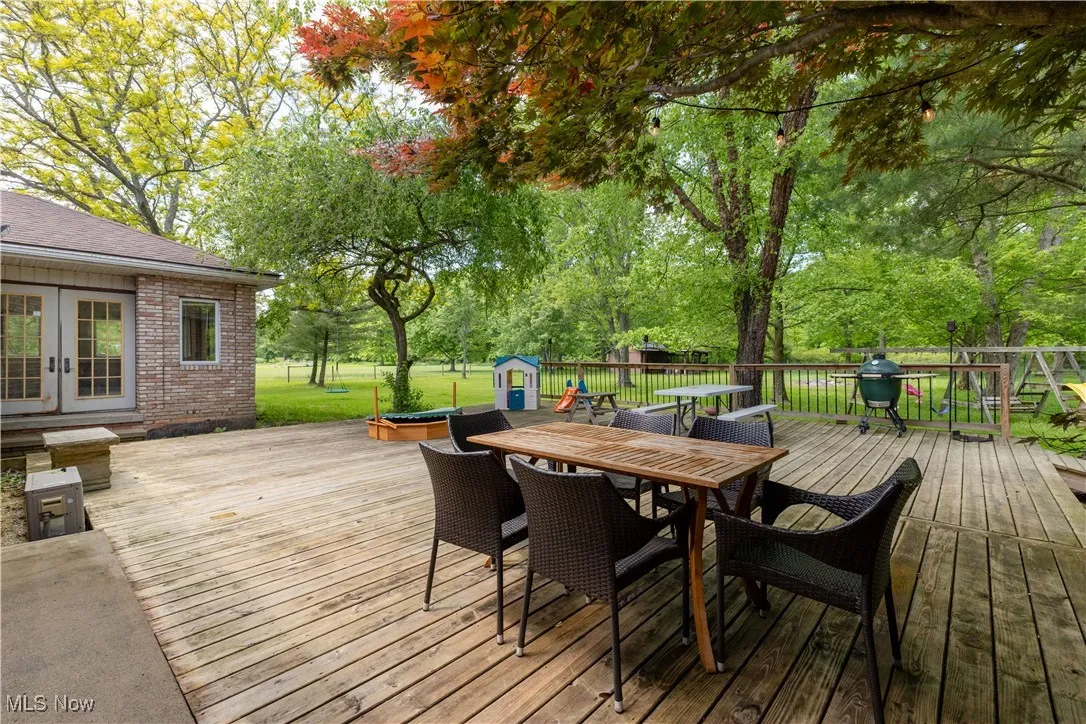 Wooden terrace featuring outdoor dining space, french doors, and view of scattered trees