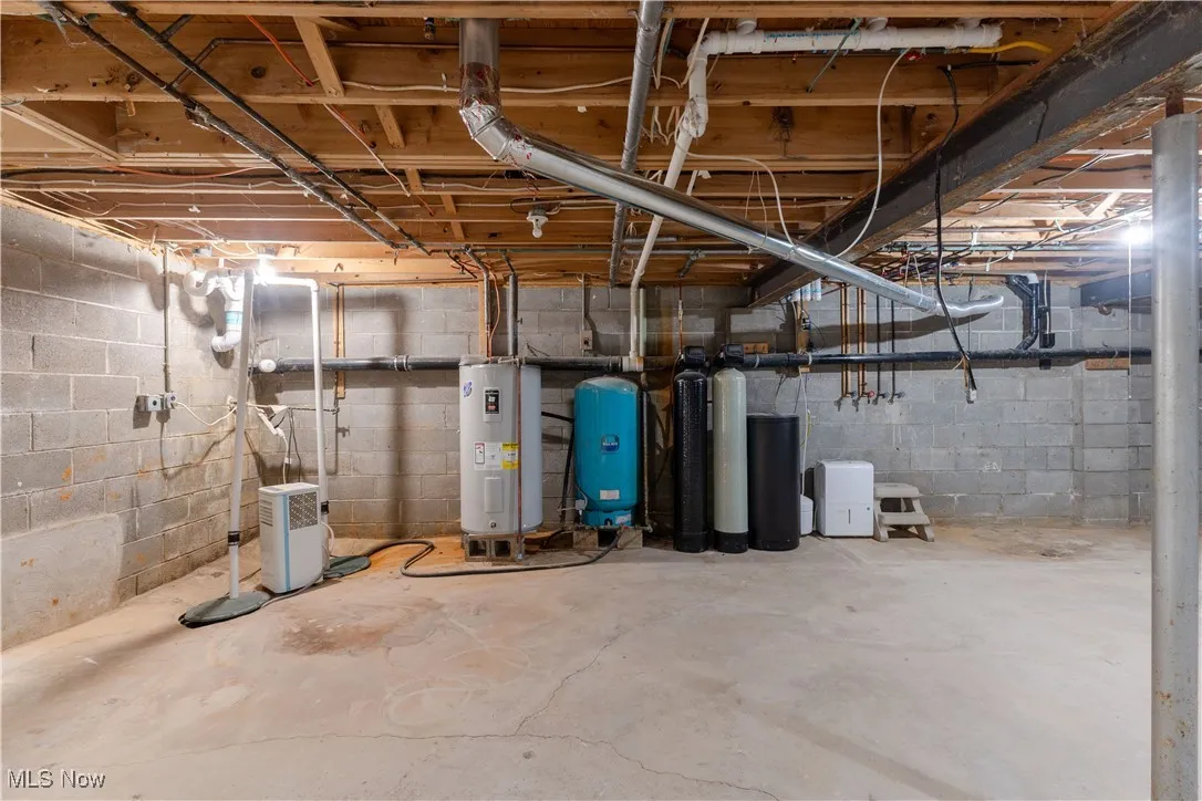 Unfinished basement with electric water heater, a water softener system, and a water pressure tank