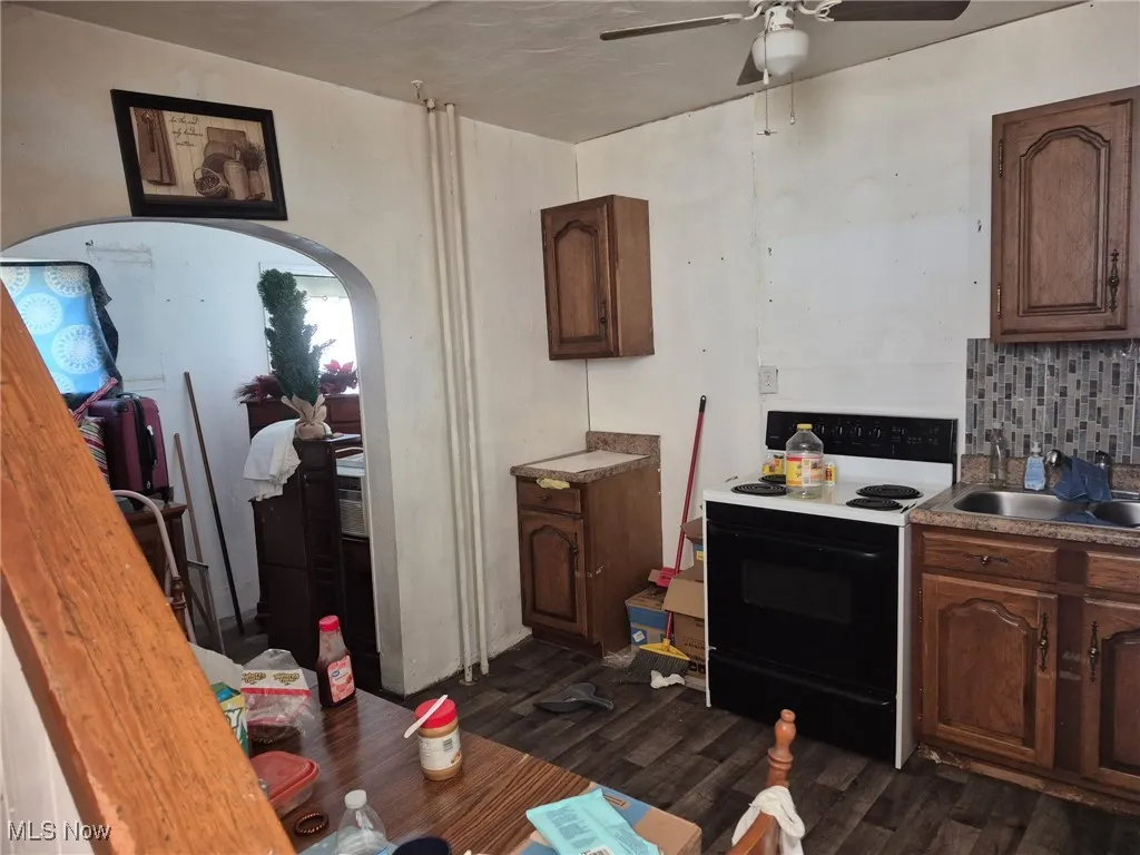 Kitchen featuring range with electric cooktop, ceiling fan, dark wood finished floors, a sink, and decorative backsplash