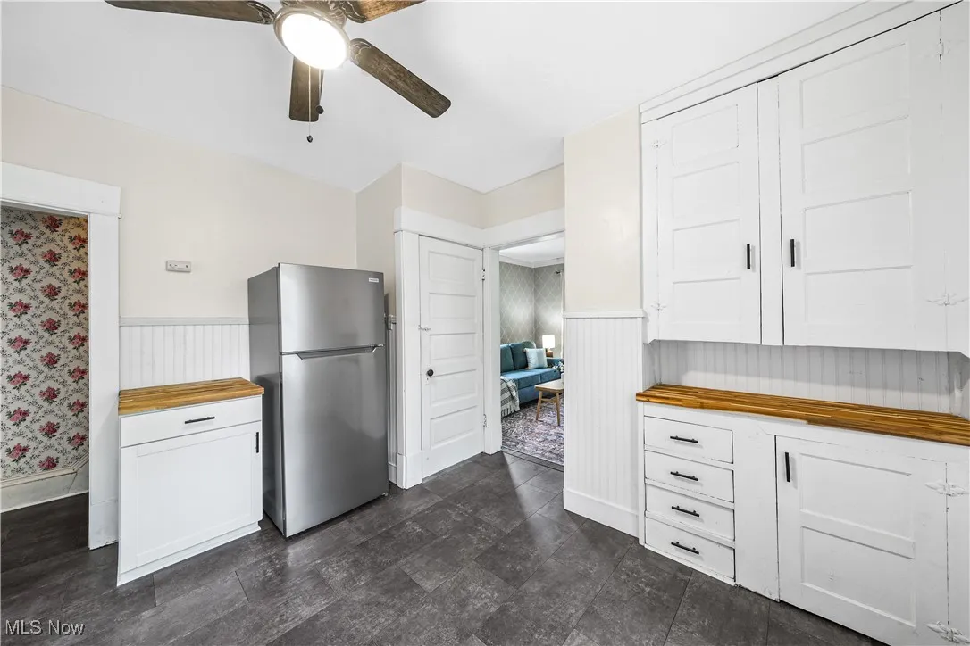 Kitchen featuring freestanding refrigerator, butcher block counters, wainscoting, a ceiling fan, and white cabinetry