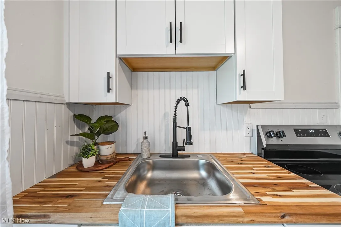 Kitchen featuring a sink, wooden counters, stainless steel electric stove, and white cabinetry