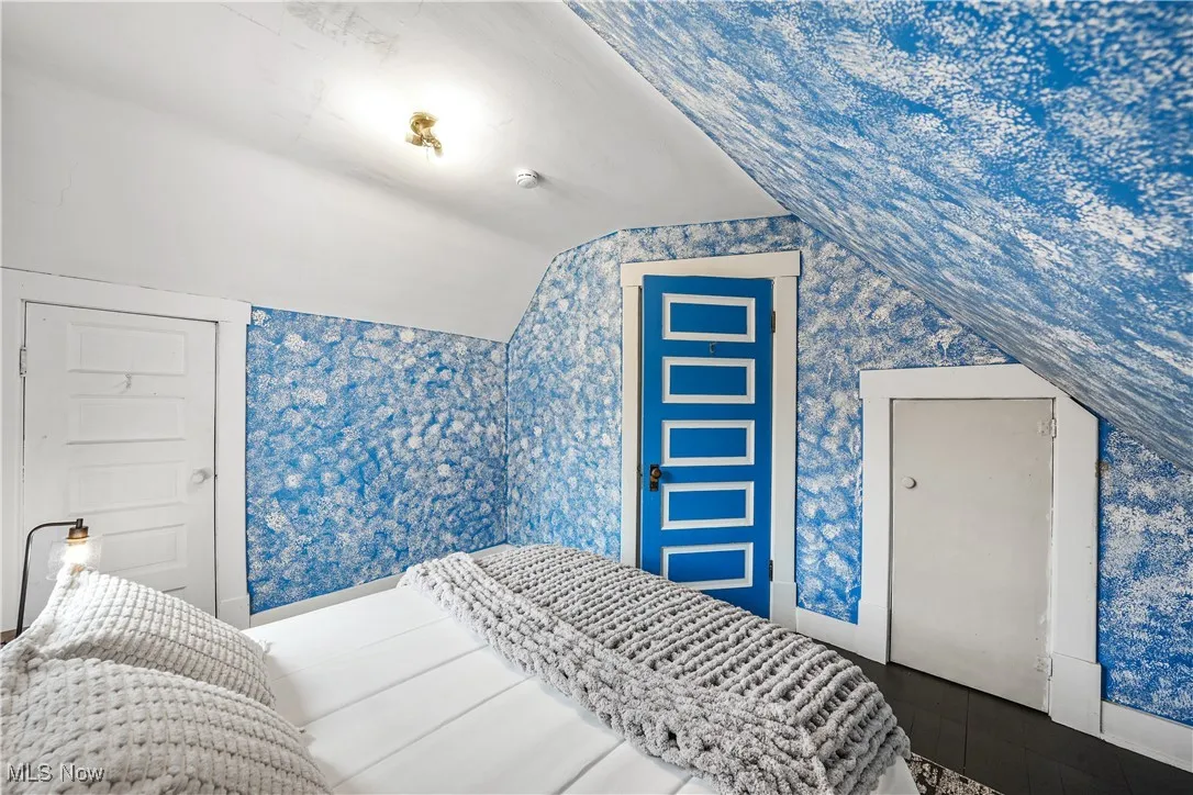 Bedroom with wallpapered walls, lofted ceiling, baseboards, and wood finished floors