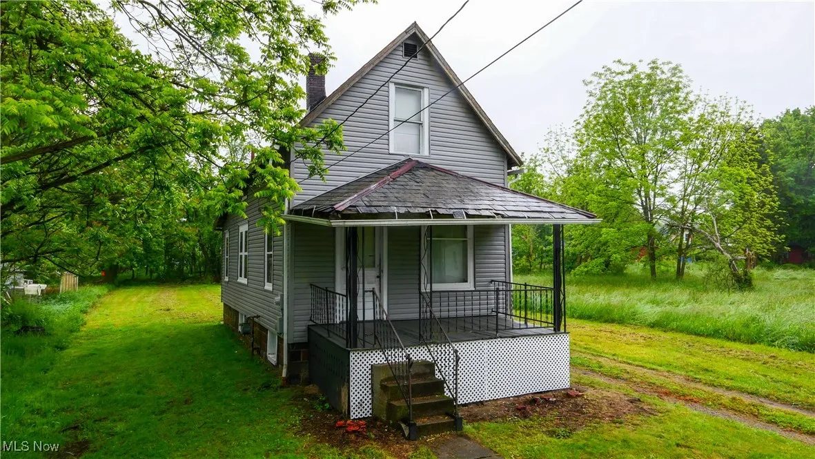 View of front of property with covered porch, a chimney, and a front yard