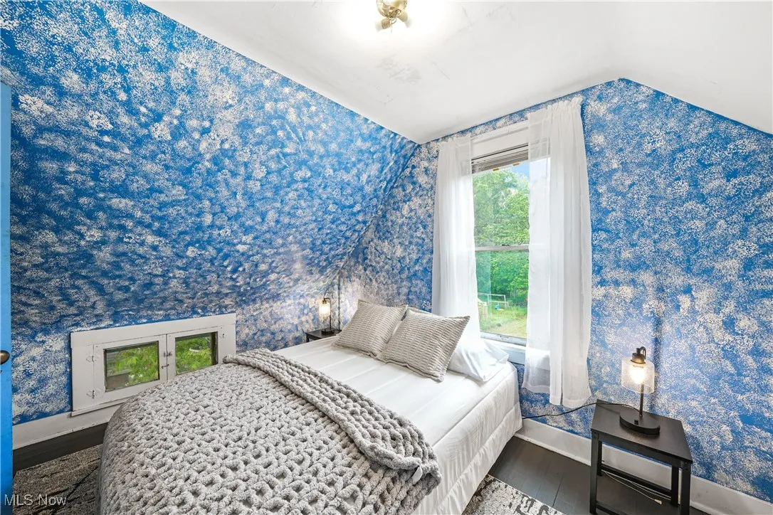 Bedroom featuring baseboards, wallpapered walls, wood finished floors, and lofted ceiling