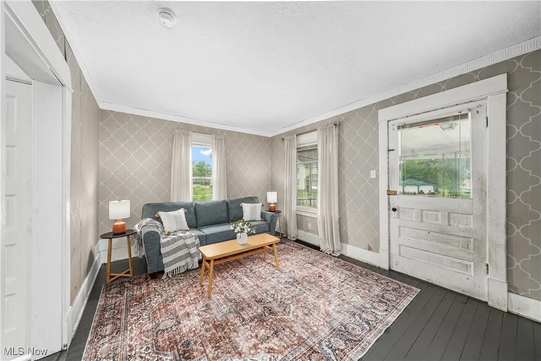 Living room featuring crown molding, dark wood-type flooring, wallpapered walls, and baseboards